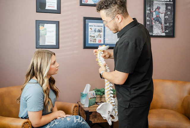 Chiropractor Eric Rivera Gesturing To Spine Model With Patient