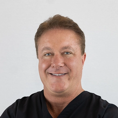 Chiropractor Charles Pray Smiling In Front Of Grey Background