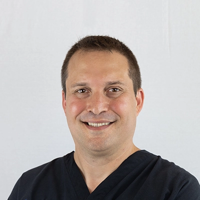 Chiropractor Jason McRae Smiling In Front Of Grey Background